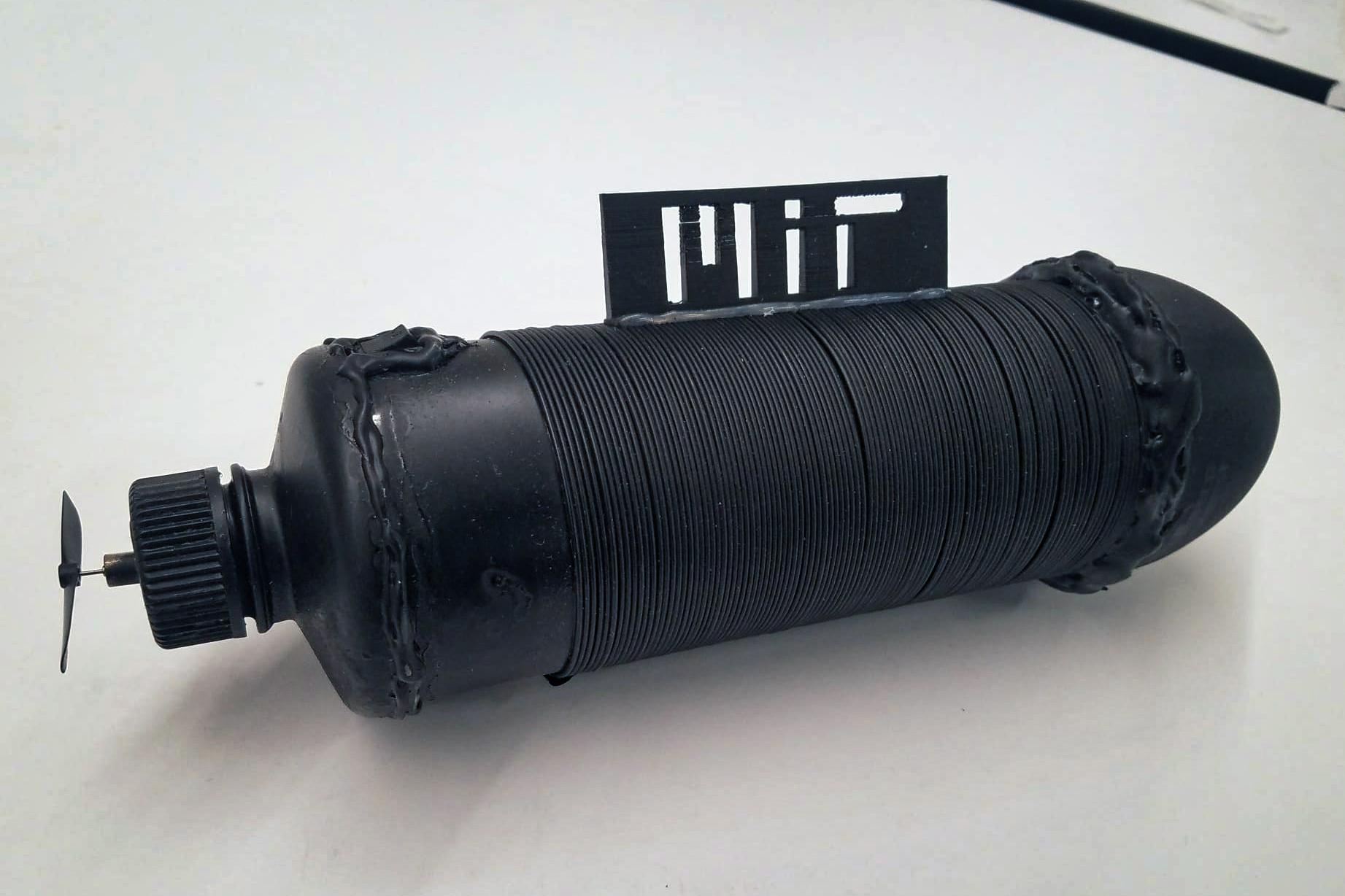 A black tube wrapped in a black wire with the MIT logo on top and a propeller at one end.