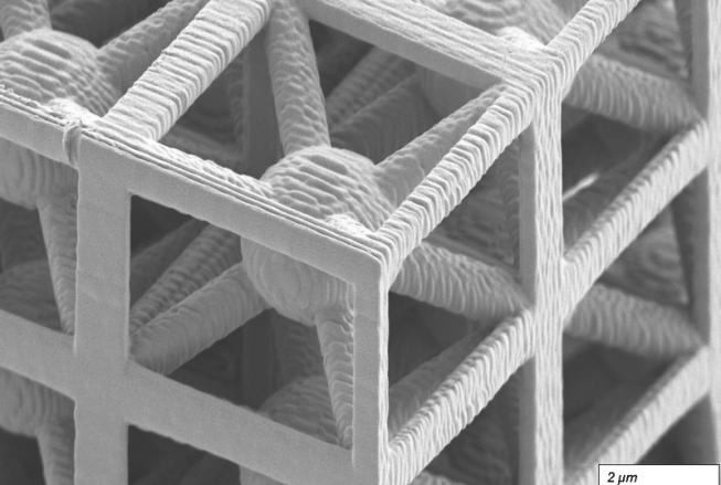 A greyscale micrograph of a latticed structure. There is a scale bar in the lower right corner noting that ~1.5 cm equates to 2 µm.