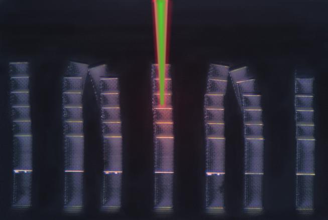 Seven architected metamaterial sample columns. The middle sample has a laser shining down upon it.