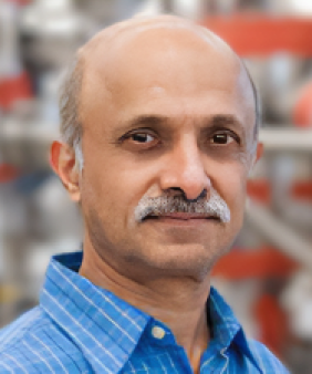 A man stands in front of a blurred background of pipes and beams